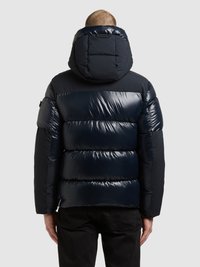 Mornarsko modra puhovka z vzorcem šivov, kapuco in sijočim zaključkom; ima široke vodoravne razdelke in elastične zapestnike.