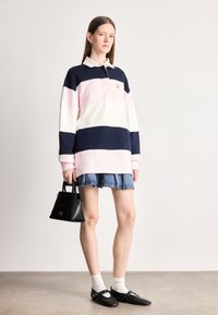 Πολυάριθος με μακριά μανίκια σε ναυτικό μπλε, ανοιχτό ροζ και λευκές ρίγες, με γιακά και κεντημένο λογότυπο. Συνδυάζεται με τζιν φούστα και μαύρη τσάντα.