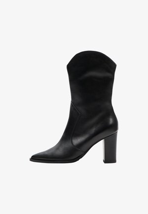 Botă de gleznă din piele neagră, cu vârf ascuțit, toc înalt și pătrat și un zăbrel puțin curbat. Textură netedă, cu detalii minime de cusătură.