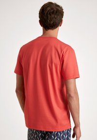 Korte mouwen ronde hals T-shirt van koraalkleurige katoenstof, met een gladde textuur en een eenvoudig ontwerp. Weergegeven op een persoon van achteren.