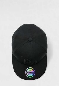 Mustas pää, jossa on litteä lippa, teksturoitu kangas ja ympyränmuotoinen holografinen tarra, jossa lukee "Alkuperäinen istuvuus", etupuolella.