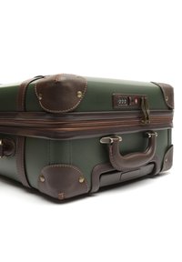 Valigia verde con dettagli in pelle marrone, hardware in bronzo e cerniere. Presenta angoli rinforzati, una maniglia superiore e una serratura a combinazione.