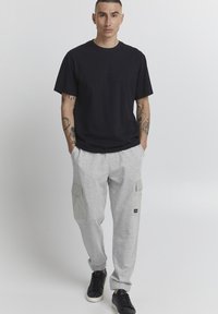 Black cotton t-shirt with round neckline. Light grey cargo sweatpants featuring two side pockets and elastic cuffs, paired with black sneakers.