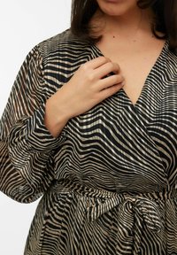 Robe à manches longues et décolleté en V en tissu noir transparent avec des rayures beiges. Dispose d'une ceinture nouée à la taille et d'un motif texturé et ondulé.
