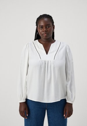 Blusa bianca a maniche lunghe con scollo a V, caratterizzata da cuciture decorative lungo il collo e polsini arricciati; tessuto liscio e leggero.
