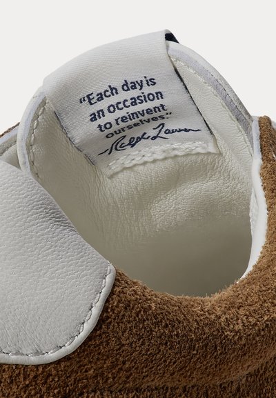 Talon de chaussure en cuir blanc avec une étiquette cousue montrant une citation de Ralph Lauren : "Each day is an occasion to reinvent ourselves."