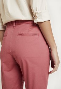 Pantalon en coton rose avec une texture lisse, doté de deux poches arrière et d'une taille mi-haute, associé à un haut crème à boutons.