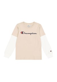 Beige T-shirt met lange mouwen en witte mouwen, met een groot marineblauw 'Champion' logo over de voorkant en een klein logo op de mouw.