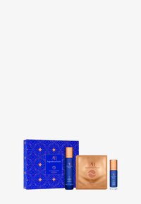 Blue box with gold geometric pattern contains three skincare products: a blue bottle with an orange pump, a gold sheet mask, and a small blue bottle.