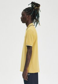 Polo giallo con rifiniture nere e bianche, caratterizzato da maniche corte e un colletto classico. Indossato con pantaloni blu navy.