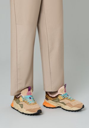 Sneakers beige e marroni con tessuto testurizzato, lacci colorati e suola spessa. Il design presenta accenti giocosi e materiali misti.