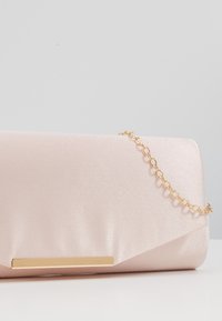 Jasnoróżowa satynowa torebka kopertowa z złotym łańcuszkiem i prostokątnym złotym akcentem na przednim klapku.