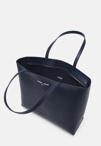 Laivastonsininen nahkainen olkalaukku, jossa on kaksi pitkää kahvaa, avoin yläosa ja vetoketjulla suljettava lokero sisällä sekä etupuolella logo.