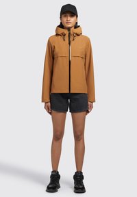 Brown waterproof jacket with a zip front, adjustable hood, and two pockets, paired with black shorts and black sneakers.