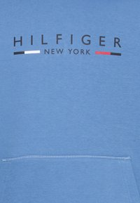 Felpa blu chiaro con scollatura rotonda, tasca frontale e lettering nero "HILFIGER NEW YORK." Presenta strisce orizzontali rosse e bianche.