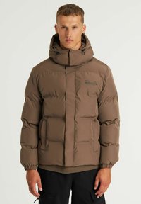 Chaqueta acolchada marrón con un alto cuello, cierre de cremallera, puños elásticos y detalles cosidos. Presenta un logotipo impreso en el pecho.
