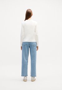 Witte langemouwen top met een ontspannen pasvorm, gecombineerd met lichtblauwe broek met wijde pijpen en beige sneakers. Minimalistisch ontwerp, gladde textuur.