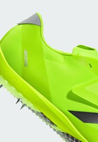 Neon green athletic shoe with a mesh upper, textured surface, and a rubber sole featuring metallic spikes for traction.