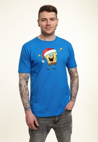 Camiseta de manga corta azul con un gráfico de un personaje amarillo alegre que lleva un sombrero de Navidad rojo. Tejido de algodón, ajuste casual.