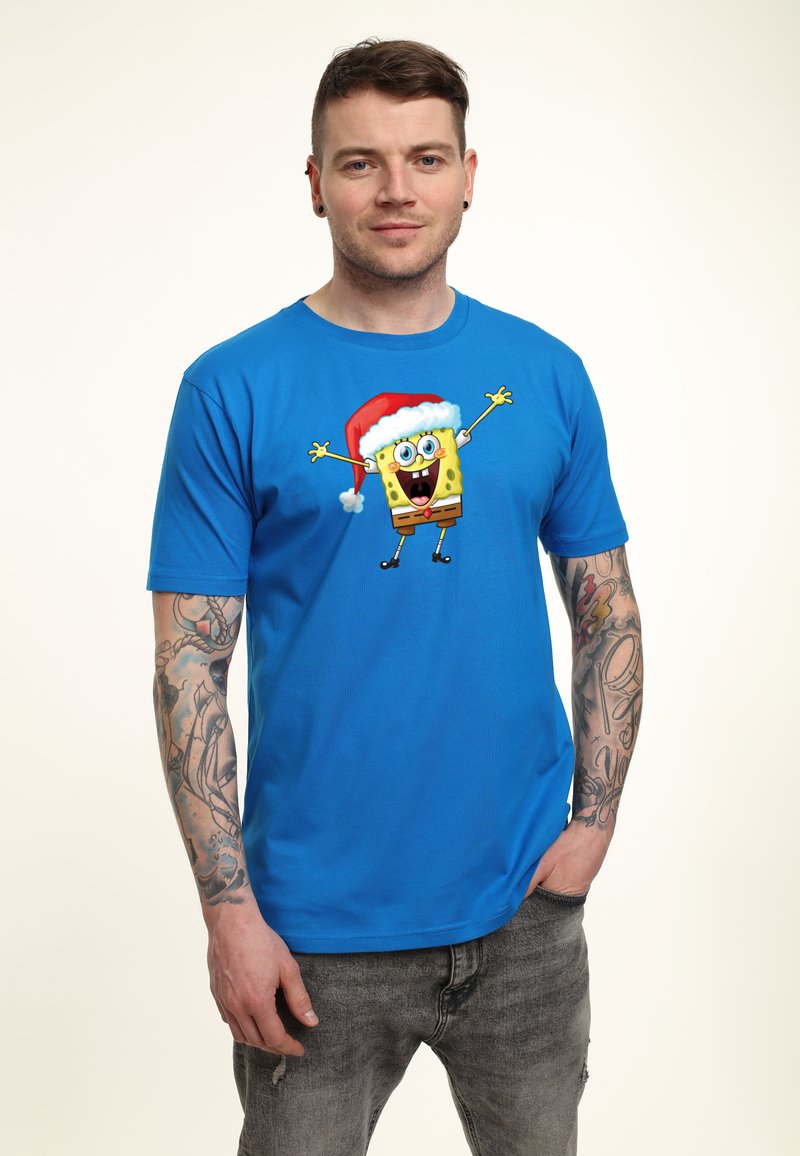 Camiseta de manga corta azul con un gráfico de un personaje amarillo alegre que lleva un sombrero de Navidad rojo. Tejido de algodón, ajuste casual.