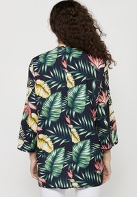 Kimono s květinovým potiskem s velkými zelenými listy a jasnými tropickými květinami na navy pozadí. Má volný střih a tříčtvrteční rukávy.