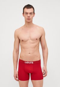 Röda bomullsboxer med vita Levi's-logotyp på midjan. Designen är åtsittande och har en slät yta.