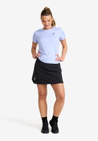 Hellblaues kurzärmeliges Hemd mit Logo, kombiniert mit einem schwarzen sportlichen Rock. Das Outfit wird mit schwarzen Sportschuhen und Socken abgerundet.