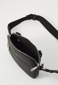 Black synthetic crossbody bag with a textured surface, silver zipper, and adjustable strap. Interior features compartments and a pocket.