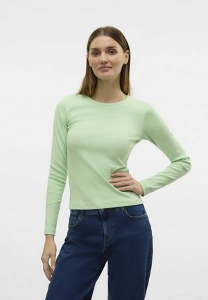 Lys grøn langærmet ribbet skjorte med rund hals, båret med mørkeblå jeans. Stofser ser blødt og tætsiddende ud.