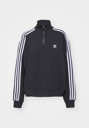Černý pulovr Adidas s bílými třemi proužky na rukávech, čtvrtkruhovým zipem u krku, žebrovanými manžetami a logem Adidas trefoil na hrudi.