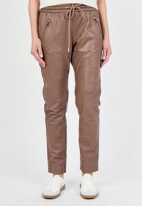 Bruna läderjoggers med dragsko i midjan, fickor med dragkedja, smalnande ben och en slät yta, tillsammans med vita sneakers.