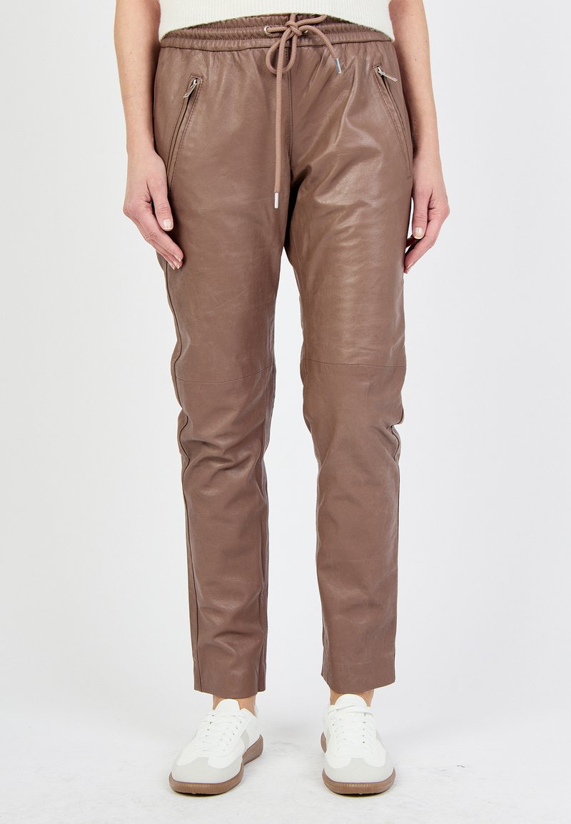 Bruna läderjoggers med dragsko i midjan, fickor med dragkedja, smalnande ben och en slät yta, tillsammans med vita sneakers.
