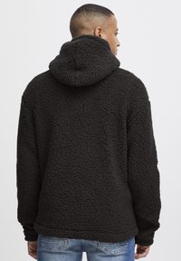 Black, fluffy fleece hoodie with a hood, featuring a textured surface. The back shows a relaxed fit, suitable for layering.