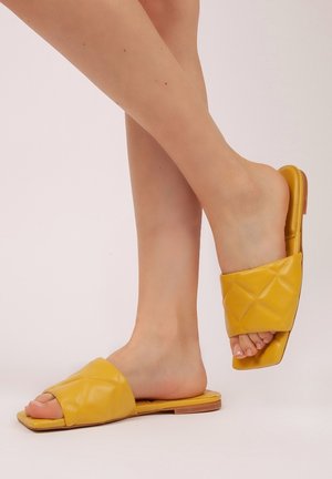 Sandalias deslizantes de cuero amarillo con un diseño superior acolchado, punta abierta, suela plana y una textura suave. Construcción ligera.