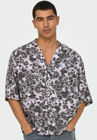 Camisa de botones de manga corta en tejido ligero, con un estampado de leopardo negro y gris sobre un fondo púrpura claro.