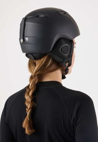 Schwarzer Helm mit glattem, mattem Finish, Belüftungsschlitzen und verstellbarem Kinnriemen. Sichtbare strukturierte Polsterung und Mesh-Akzente.