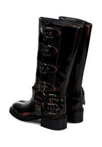 Botas de cuero negras hasta la mitad de la pantorrilla con múltiples hebillas y correas plateadas, tacones gruesos y un acabado brillante, mostradas desde un ángulo trasero.