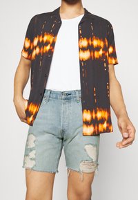 Short-sleeve shirt in black with orange tie-dye pattern, paired with light blue distressed denim shorts featuring frayed edges and patches.