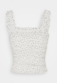 Vit topp med mörka prickar, med en smockad design och volangärmar, vilket ger ett strukturerat och texturerat utseende.