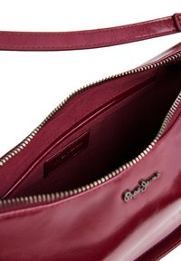 Κόκκινη δερμάτινη τσάντα χειρός με φερμουάρ από πάνω, ορατή εσωτερική τσέπη από ύφασμα και ανάγλυφο λογότυπο μάρκας στην μπροστινή πλευρά.
