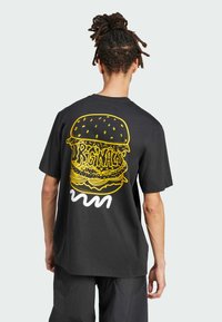 T-shirt in cotone nera con una grande grafica di un hamburger giallo e il testo "Originals" sulla schiena, con una vestibilità ampia e maniche corte.