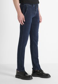 Jeans de denim azul oscuro con un corte recto, talle medio y costuras en contraste, combinados con brillantes zapatos negros de cordones.