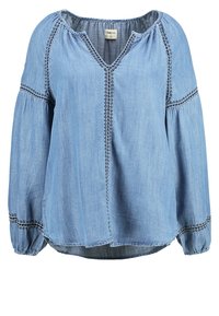 Blouse bleu clair à manches longues avec col en V, encolure froncée et couture noire décorative le long des manches et des coutures avant.