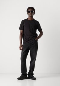 Tricou negru, blugi negri din denim și adidași negri. Modelul poartă ochelari de soare închiși la culoare. Design simplu, cu o croială lejeră și culori solide.