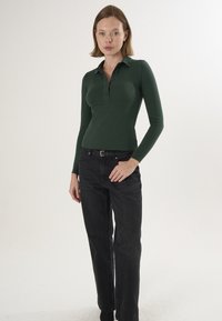 Grøn langærmet polo med tre knapper, kombineret med højtaljede sorte jeans. Blødt stof med en figursyet pasform.