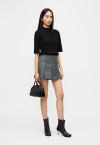 Μαύρο ριμπ κοντομάνικο τοπ σε συνδυασμό με γκρι πλισέ φούστα που έχει διακοσμητικά κουμπιά στη μία πλευρά και μαύρα μποτάκια αστραγάλου. Μικρή μαύρη τσάντα χειρός.