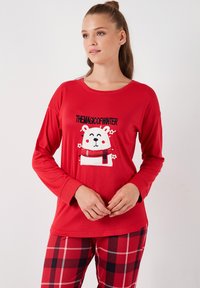 Punainen pitkähihaisen paita, jossa on napapiirin karhun grafiikka, brodeeratut yksityiskohdat ja teksti "TALVEN TAIKA". Yhdistetty ruudullisiin pyjamahousuihin.