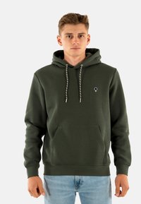 Sudadera de color verde oscuro hecha de un tejido suave, con un bolsillo tipo canguro, cordones con detalles en plata y un pequeño logo de un árbol en el pecho.