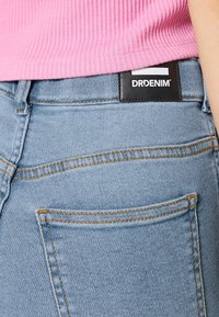 Vaaleansiniset farkut sisältävät mustan DRDENIM-logon takana, näkyvää tikkausta ja klassisen taskusuunnittelun.