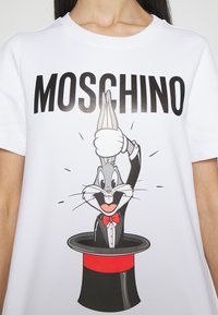 Personne portant un t-shirt blanc avec le texte « "Moschino" » et Bugs Bunny en smoking sortant d’un chapeau de magicien imprimés sur le devant.